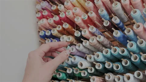 Row of colorful thread spools. Female hand with manicure chosing and looking for Stock Footage 107964974