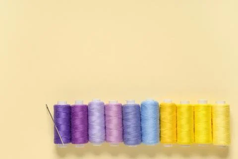 Row of colorful thread spools with needle on beige background 写真素材