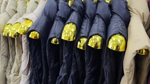 Row of colorful winter puffer jackets on golden hangers inside clothing store, Stock Footage 341658118
