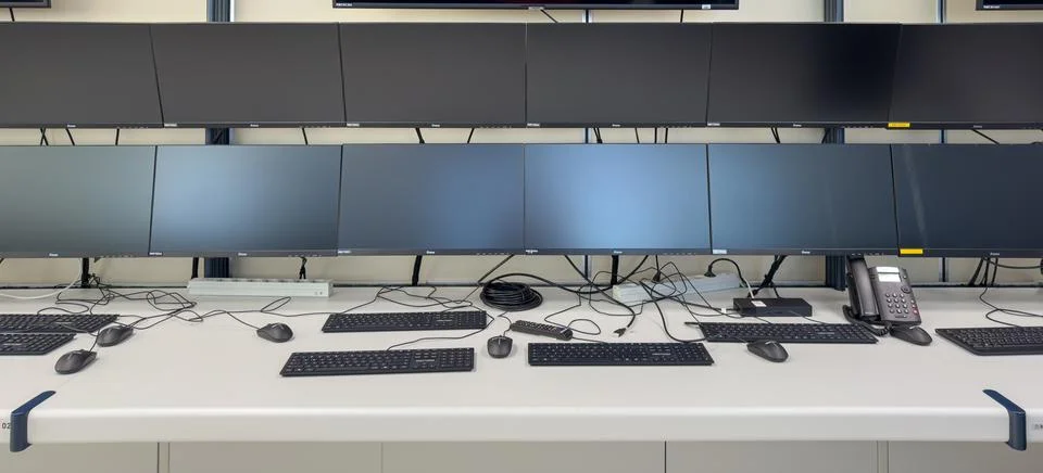 A row of computer monitors are mounted to the wall above a desk with keyboa.. Фото