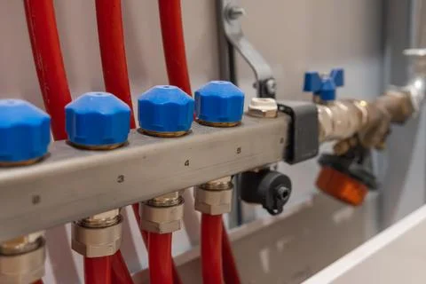 Row of connected heating pipes with valve caps on manifold. Fotos Stock