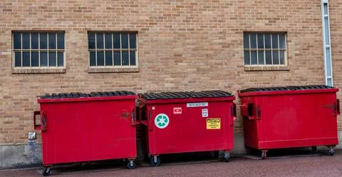 Row of covered garbage bins along a brick wall in a back alley Stock Photos