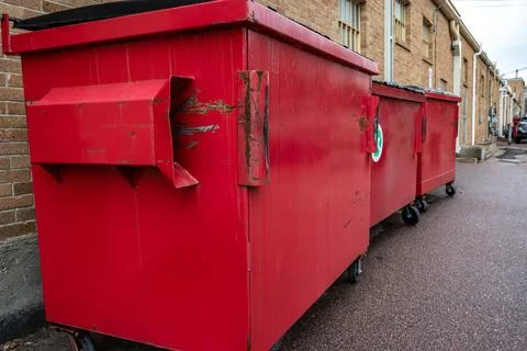 Row of covered garbage bins along a brick wall in a back alley Stock Photos