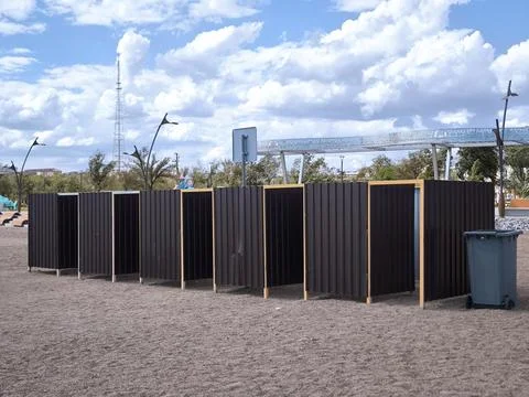 A row of dark changing cabins on a sandy beach under a cloudy sky Stock Photos