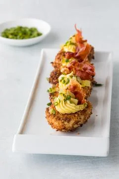 A row of deep fried gourmet deviled eggs garnished with chives and prosciutto. Stock Photos