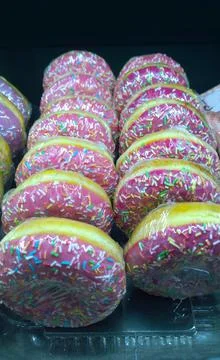 Row of donut with pink sugar glaze and colorful pastry sprinkles in store Stock Photos