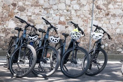 A row of electric bicycles with helmets parked beside a traditional stone w.. Stock Photos