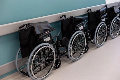 A row of empty folded wheelchairs along a corridor with a blue wall Stock Photos