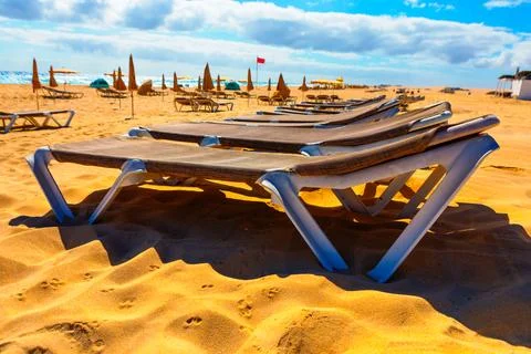 Row of empty lounge chairs on a sandy beach Stock Photos