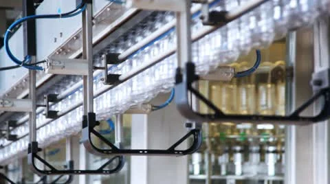 Row of empty plastic bottles move at factory, behind in blur rotates device to Stock Footage