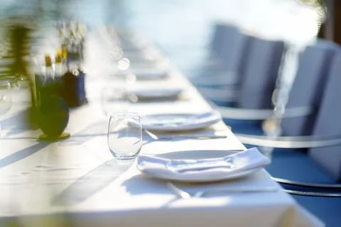 A row of empty plates on a long table with a white tablecloth. A table in a M Stock Photos