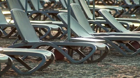 Row of empty sun beds on sandy beach, bathed in soft early morning light, resort Stock Footage 329622621