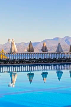 Row of empty sunbeds by the pool and the sea in the morning at dawn. Comforta Stock Photos