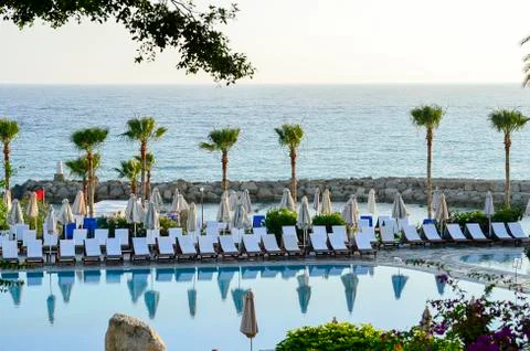 Row of empty sunbeds by the pool and the sea at sunset Stock Photos
