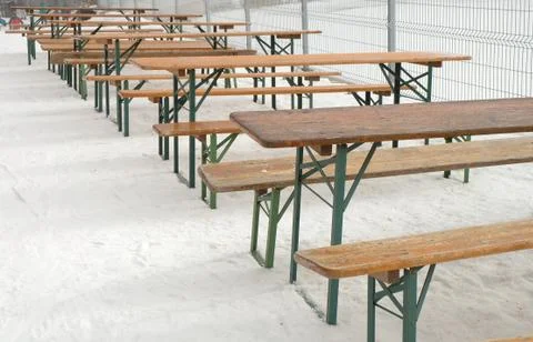 Row of empty tables and benches standing on snow at restaurant in winter Stock Photos