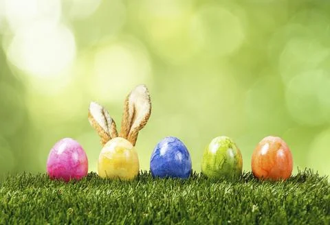 A row of five colorful easter eggs on green grass with bunny ears in Springtime Foto stock