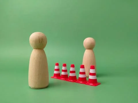 A row of five red and white traffic cones separates two wooden peg figures .. 库存照片