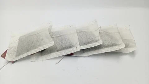 Row of Five Square Tea Bags with Strings and Red Tags on a White Surface Foto stock