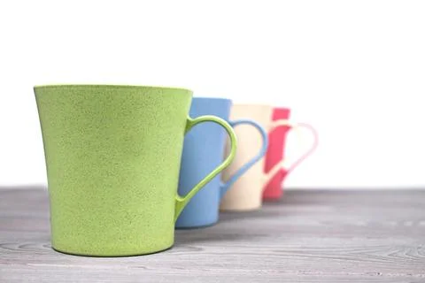 A row of four different-colored plastic mugs on a wooden table on a white bac Stock Photos