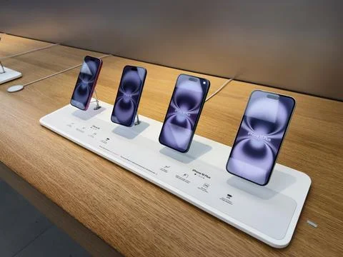 Row of four iPhone 16 Plus devices on a white display pedestal in a retail sh Stock Photos