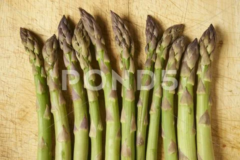 A row of green asparagus spears on a wooden board Stock Photos