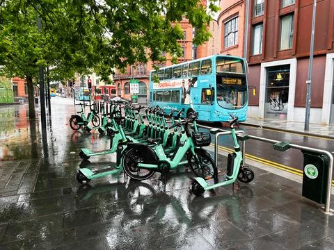 Row of green shared Bolt e scooters and bikes parked at a wet city docking .. Stock Photos