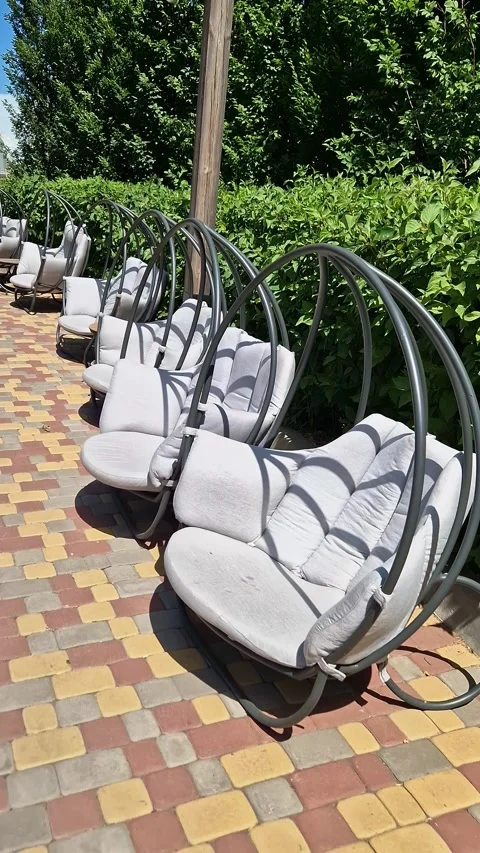 Row of Grey Hanging Egg Chairs on a Colorful Paved Outdoor Patio Stock Footage 339085175