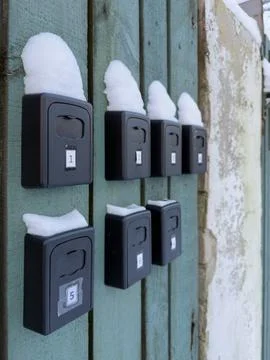 Row of key lock boxes with snow on apartment wall Stock Photos