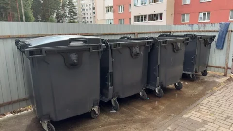 Row of large grey wheeled garbage bins lined up near a metal fence Vídeo Stock 339366516