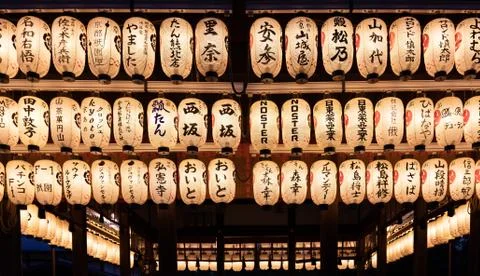 A row of lit lanterns hanging from a roof of a japanese temple Stock Photos