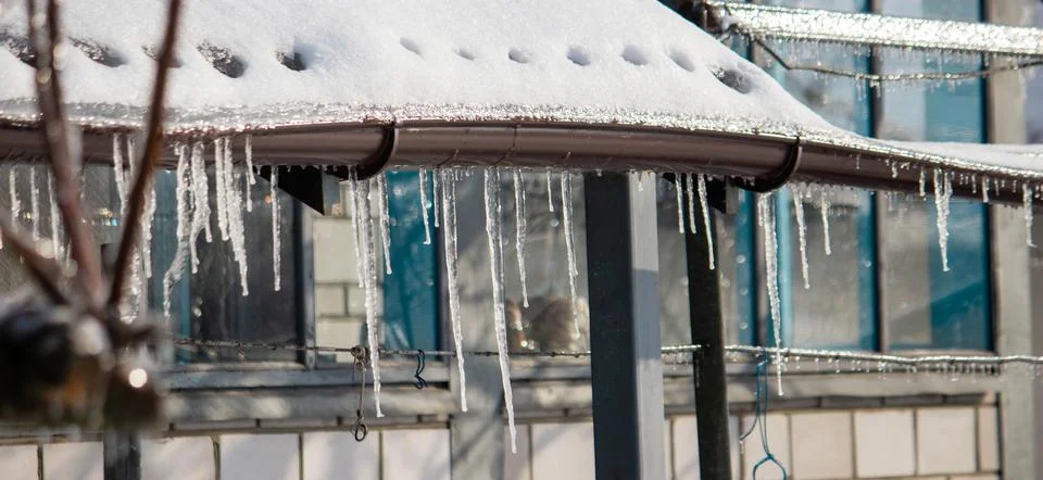 Row of long sharp icicles hanging from the roof edge in winter. Stock Photos