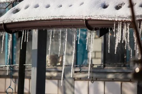 Row of long sharp icicles hanging from the roof edge in winter. Stock Photos