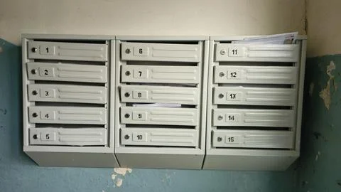 Row of metal mailboxes mounted on peeling wall, vintage stairwell lighting, c Stock Photos