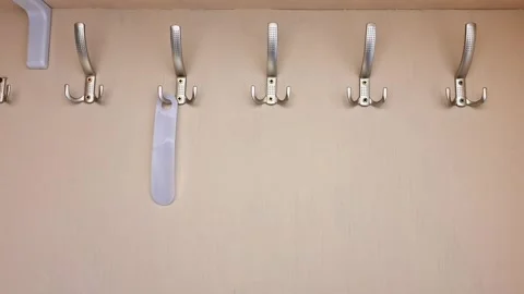Row of Metallic Coat Hooks with Hanging White Items on Beige Wall Stock Footage 331496644