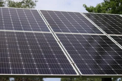 Row of modern solar panels on a background of trees and cloudy sky Stock Photos