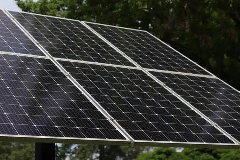 Row of modern solar panels on a background of trees and cloudy sky Stock Photos