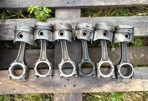 A row of old, rusted engine pistons are sitting on a wooden platform Stock Photos