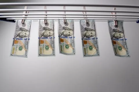 Row of one hundred dollar bills hanging on white drying rack Photos
