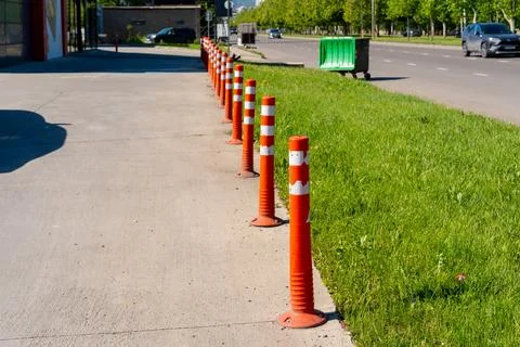 Row of orange traffic bollards lining a concrete sidewalk next to a grassy .. Stock Photos
