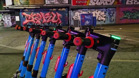 Row of parked shared electric scooters against a graffiti wall on a city st.. Stock Footage 345685044
