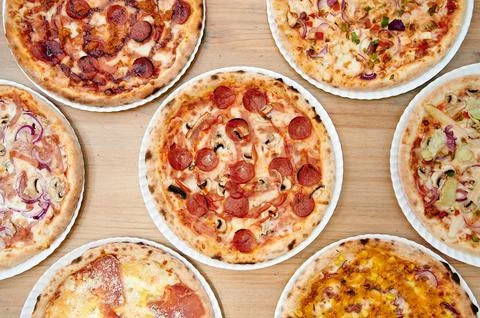 A row of pizzas with different toppings Stock Photos