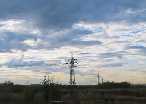 A row of power lines in a field under a cloudy sky Stock Photos