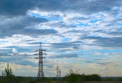 A row of power lines in a field under a cloudy sky Foto stock