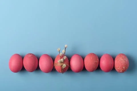 Row of red Easter eggs on blue background, centerpiece egg tied with twine an Stock Photos