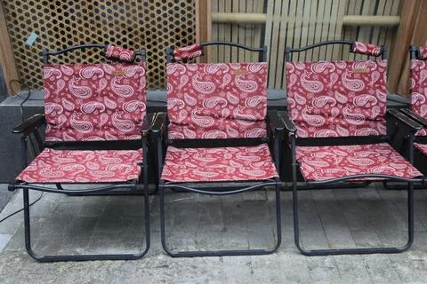 Row of red patterned folding chairs arranged in outdoor seating area along .. Stock Photos