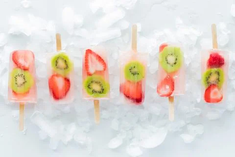 A row of refreshing strawberry kiwi popsicles on a bed of ice. Stock Photos