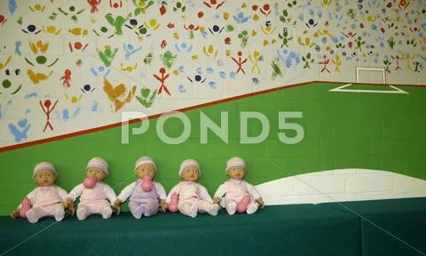Row of sitting baby dolls in front of painted wall (abstract soccer stadium) Stock Photos