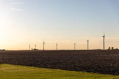 Row of Small Wind Turbines Facing Away From Sun at Sunset Across an Empty Field Stock Photos