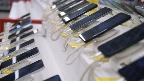 A row of smartphones is displayed on a white table in an electronics store Stock Footage 312796962