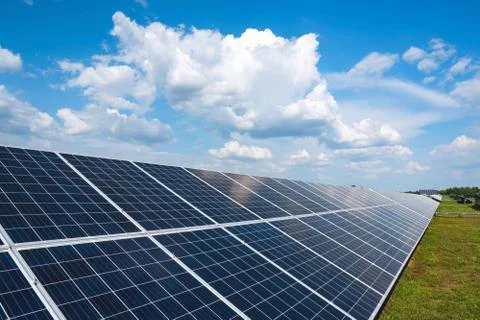 A row of solar panels in a field with clouds and a blue sky. Stock Photos
